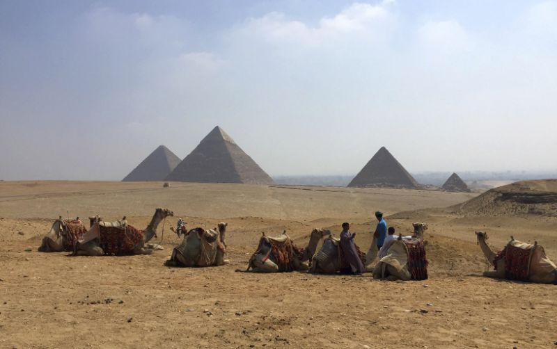 FILE - In this Aug. 30, 2015, file photo, camels rest between rides with their owners against the backdrop of the pyramids in Giza, Egypt. Archaeologists in Egypt say they have discovered a 4,400-year-old tomb near the pyramids outside Cairo. Egypt’s Antiquities Ministry announced the discovery Saturday and said the tomb likely belonged to a high-ranking official known as Hetpet during the 5th Dynasty of ancient Egypt. (AP Photo/Courtney Bonnell, File)