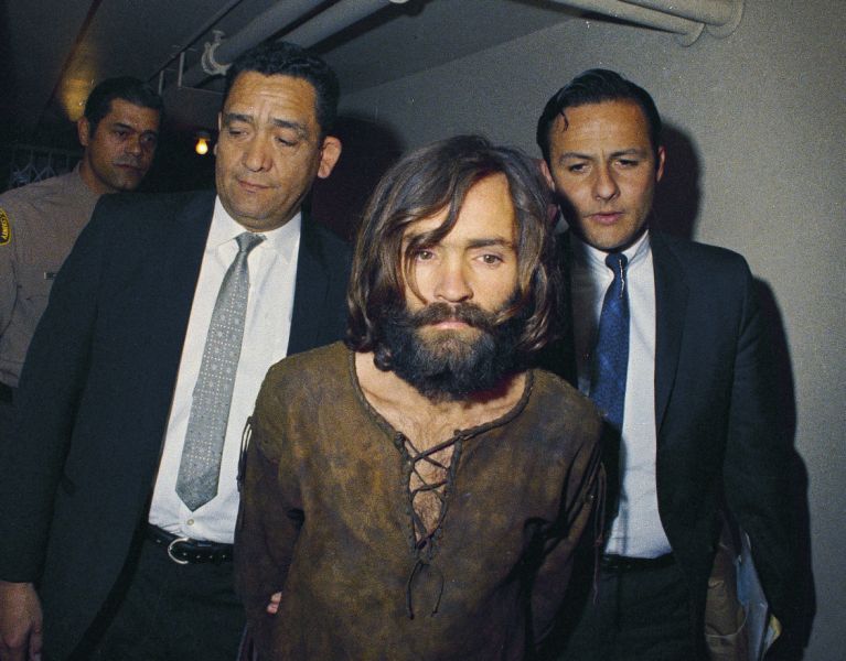 FILE - In this 1969 file photo, Charles Manson is escorted to his arraignment on conspiracy-murder charges in connection with the Sharon Tate murder case. The corpse of Manson will remain in a morgue for at least another month before would-be heirs can argue in court over who gets his remains. A Kern County Superior Court commissioner on Wednesday, Jan. 31, 2018, set a March 7 hearing in the dispute. (AP Photo, File)