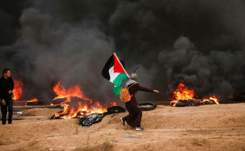 A woman runs with a Palestinian flag during clashes along the Gaza Strip border fence with Israel on October 26, 2018 (AFP Photo/MAHMUD HAMS)