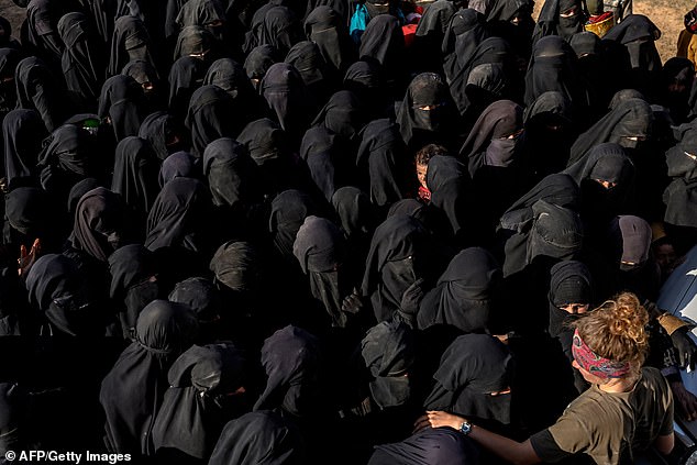 All in black: Dozens of women covered in black are waiting for bread and water after fleeing ISIS's last holdout - the town of Baghouz