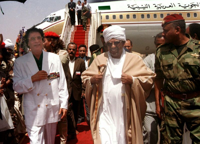 FILE - In this May 10, 2001, file photo, Libyan leader Moammar Gadhafi , left, is greeted by President Omar El-Bashir, center, upon his arrival in Khartoum for a two-day visit to Sudan. Tens of thousands of Sudanese were making their way to the center of the country’s capital on Thursday, April 11, 2019, cheering and clapping in celebration as two senior officials said the military had forced longtime autocratic President Omar al-Bashir to step down after 30 years in power. (AP Photo/Abdel Raouf, File)