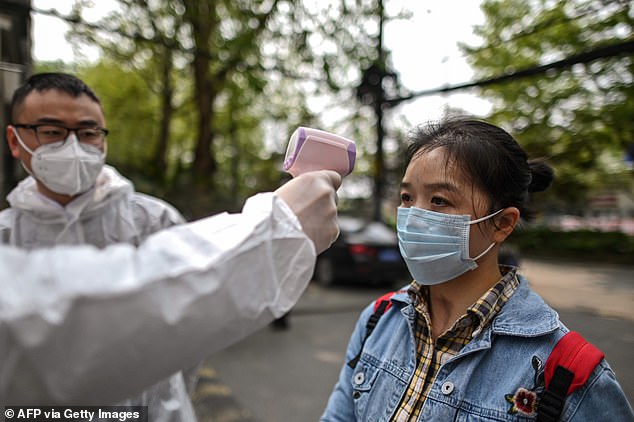 A man wearing a protective suit checking a woman's temperature next to a residential area in Wuhan today