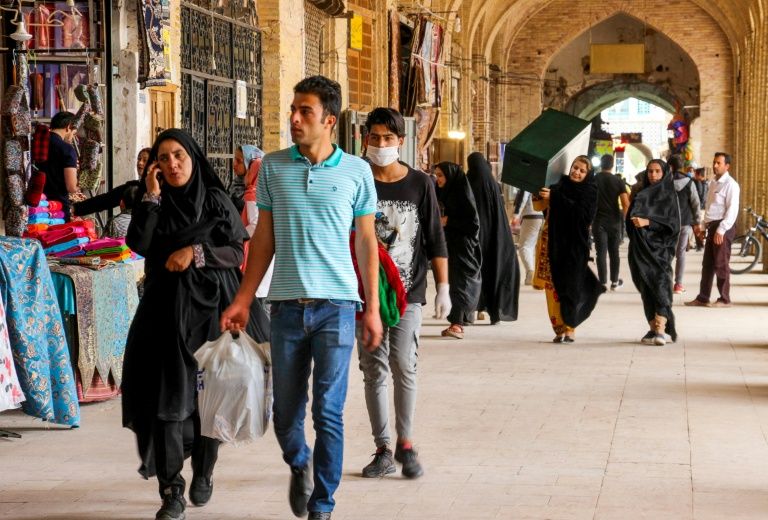 Iranians, some wearing personal protective equipment, walk past shops in the southeastern city of Kerman (AFP Photo/)
