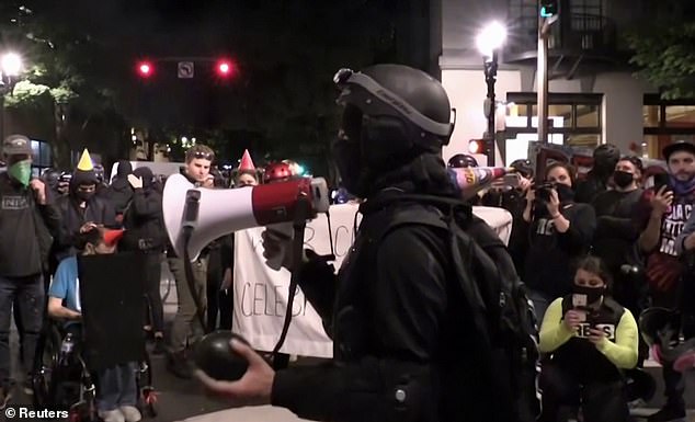 A man with a megaphone and clutching something in his left hand speaks to the crowd, which had blocked a street in the north of Portland