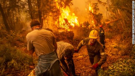 Firefighter and volunteers use a water hose near a burning blaze trying to extinguish a fire in the village of Glatsona on Evia island, on August 9.