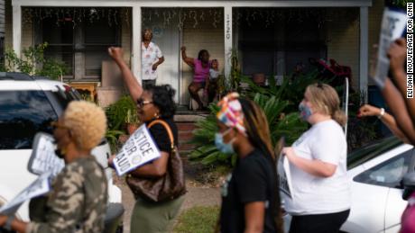 Sadie Rhone, standing at rear left, watches as marchers pass by her home in Brunswick.