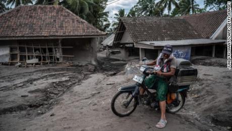 A man rides a bike past damaged homes at Sumber Wuluh village in Lumajang on December 6, 2021.