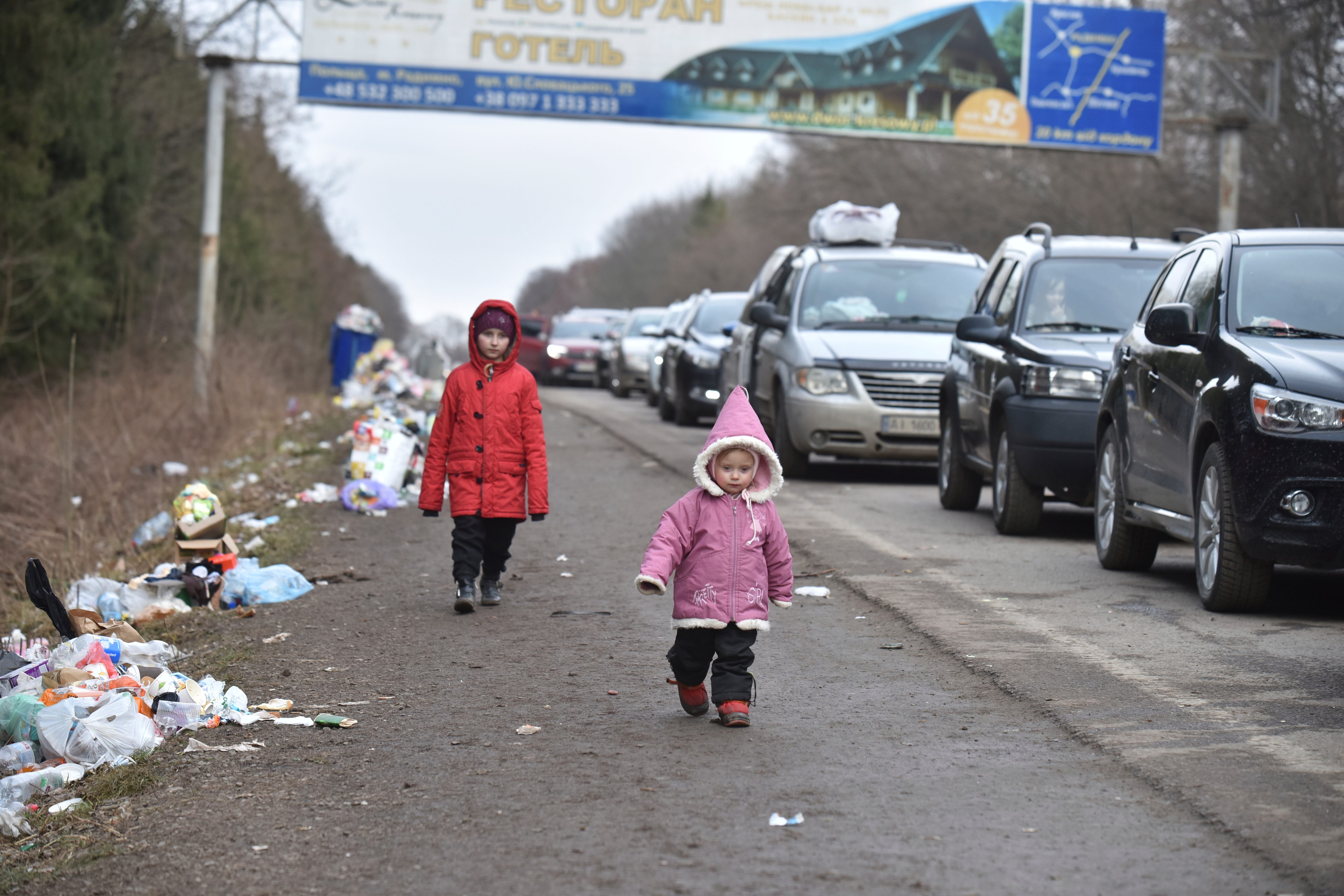 Children walk past a queue of cars heading to the Poland border near Shehyni, western Ukraine, Tuesday, March 1, 2022.