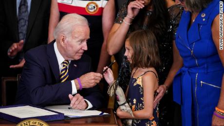 U.S. President Joe Biden hands a pen to Brielle Robinson, the daughter of Sgt. 1st Class Heath Robinson, as her mother, Danielle Robinson, stands by during a signing ceremony for "the Sergeant First Class Heath Robinson Honoring our Promises to Address Comprehensive Toxics (PACT) Act of 2022," in the East Room of the White House in Washington, U.S., August 10, 2022. REUTERS/Kevin Lamarque