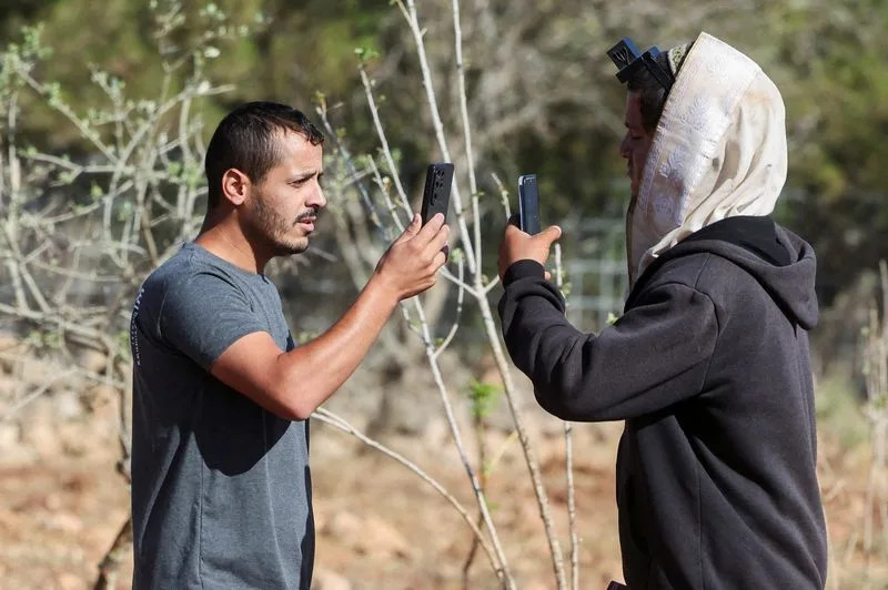 Yousef Hassan whose house was been encircled by militant settlers and later taken over by the military, films an Israeli settler