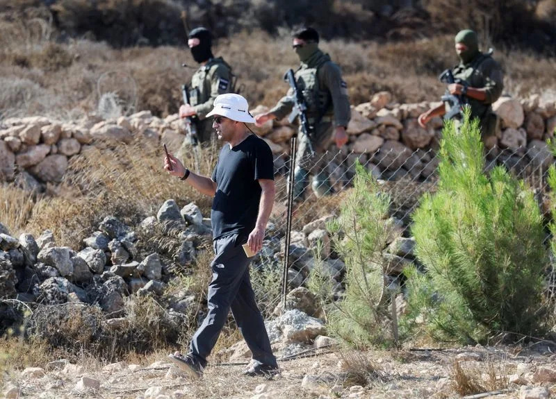 Loui Ridi, a Palestinian-American whose house has been besieged by settlers for over a week, films his property as Israeli soldiers walk on the road behind him