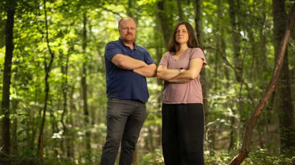 Two people standing in a wooded area