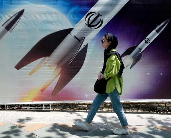A woman walks past a banner showing missiles being launched, in northern Tehran, Iran. (AP)