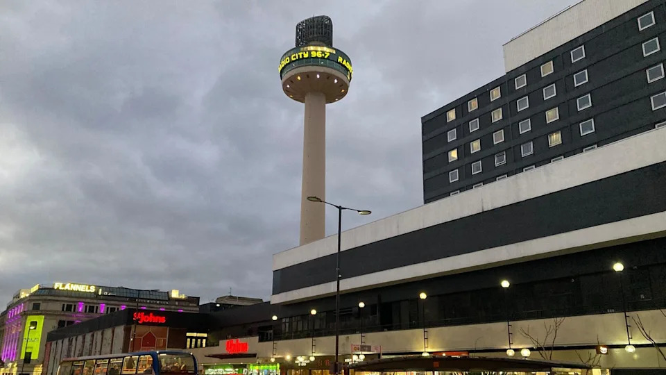 St Johns Beacon against a cloudy sky with St John centre building at ground lever lit up with red lights.