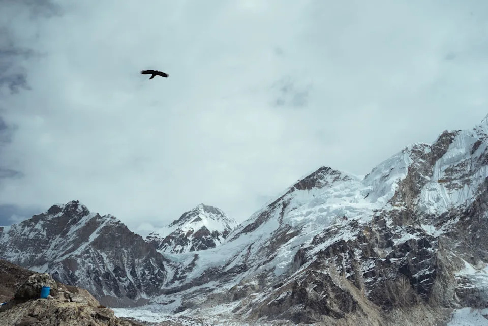 GORAKSEHP, NEPAL - OCTOBER 12: A crow flies in the sky against the Sagarmatha mountain range; a small blue trash bin has been left of the edge of the Khumbu glacier on October 12, 2024 in Gorakshep, Sagarmatha Region, Nepal. The growing popularity of trekking in Nepal has resulted in various forms of pollution spoiling the fragile ecosystem. Gorakshep is the last human settlement on the Nepal side before trekkers arrive at Everest Base Camp just 3.5km away. Here, waste management issues due to trekking tourism are apparent with plastic bottles and debris from lodges and restaurants dumped just meters from the town centre. Early in the autumn trekking season, Everest Base Camp itself also shows signs of waste mismanagement. (Photo by Mailee Osten-Tan/Getty Images)