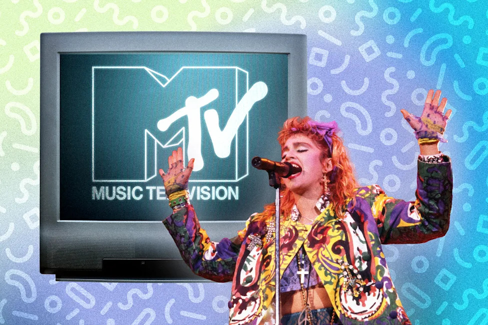 Madonna singing at a mic in the 1980s in front of a TV screen with the MTV logo on it. 
