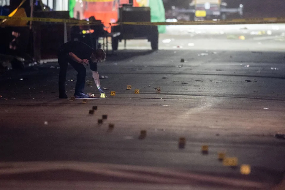 An investigator with the Tallahassee Police Department uses a flashlight to look over dozens of evidence markers that snake down Perry Street behind Florida A&M University's Bragg Memorial Stadium as the TPD investigates a mass shooting Saturday, Oct. 24, 2026.